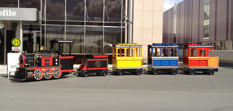 Kleine Bimmelbahn mit Lok und drei bunten Wagen vor einem Gebäude