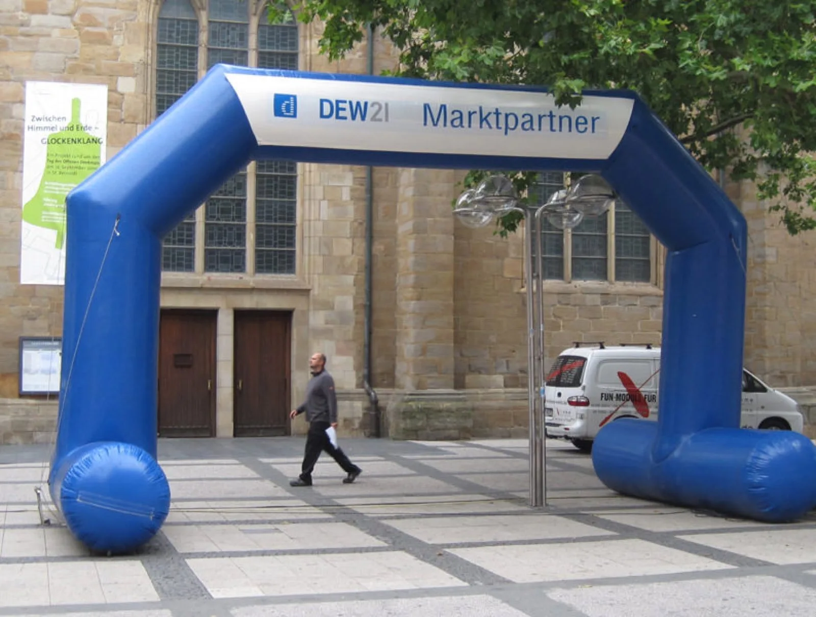 Blauer aufblasbarer Werbe-Torbogen mit Aufdruck „DEW21 Marktpartner“ vor einer Kirche