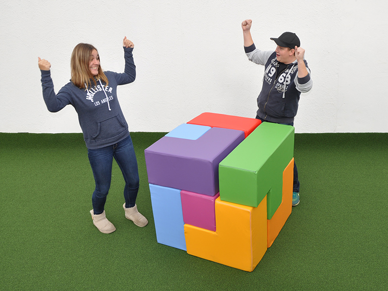 Zwei Personen jubeln neben einem großen bunten Würfel aus Tetris-Steinen