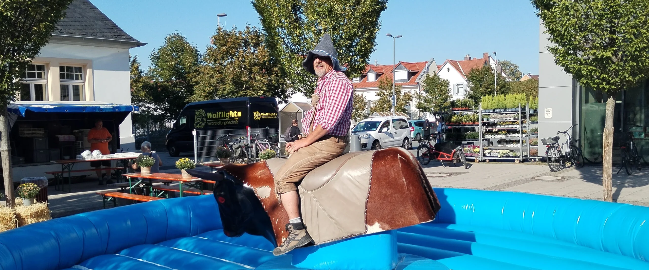 Gast mit Hut reitet auf dem Bayern-Rodeo über dem blauen Luftkissen, dahinter ein Straßenfest