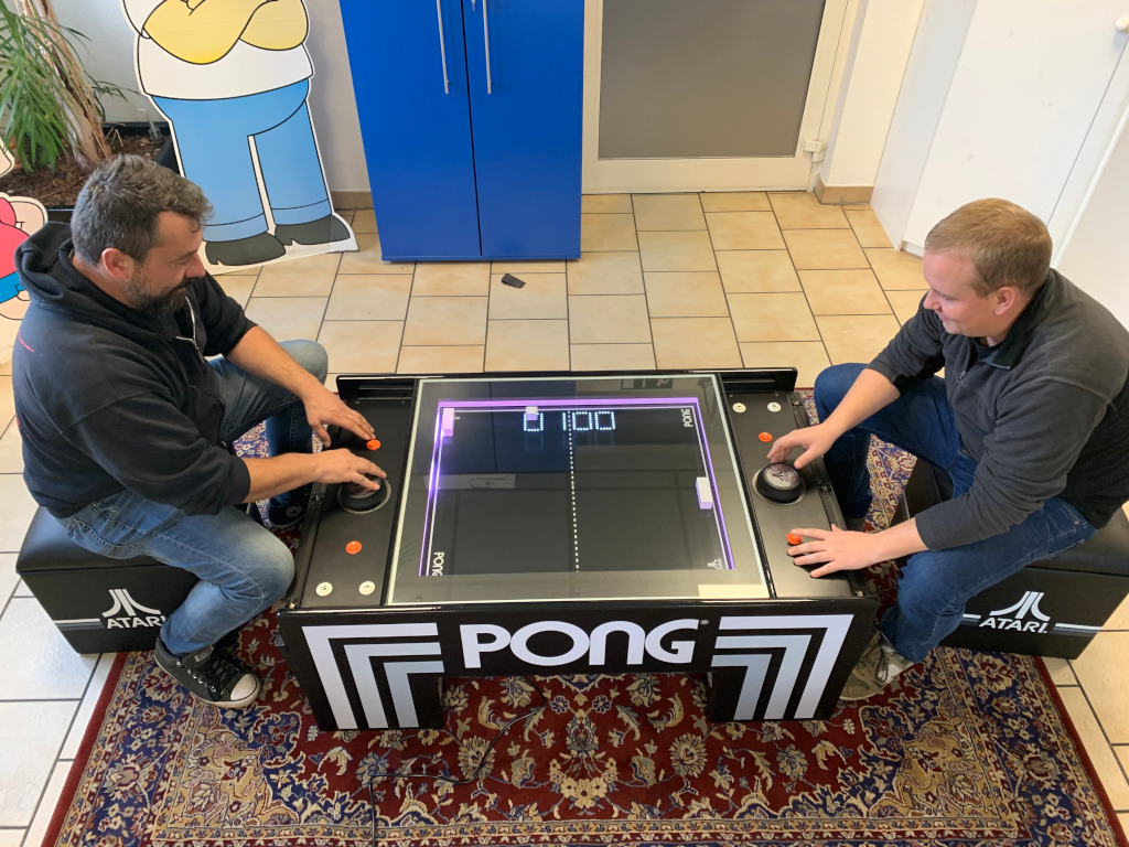 Zwei Männer spielen am beleuchteten PONG-Tischgerät