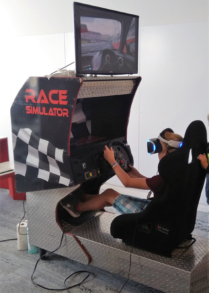 Person mit VR-Brille im Rennsitz eines Race-Simulators vor einem Bildschirm