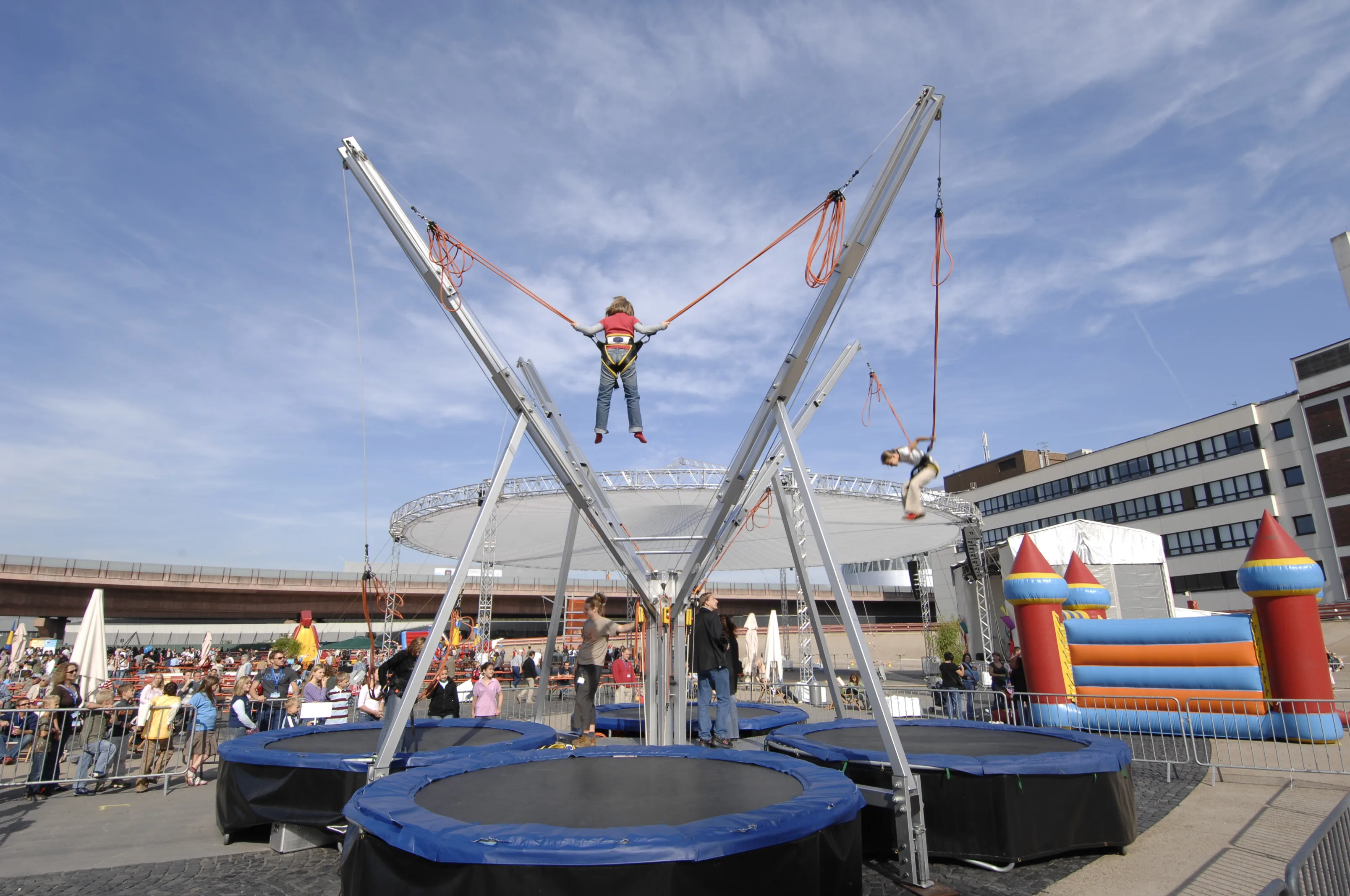 Bungee-Trampolin-Anlage auf einem Platz, im Hintergrund Hüpfburg und Publikum