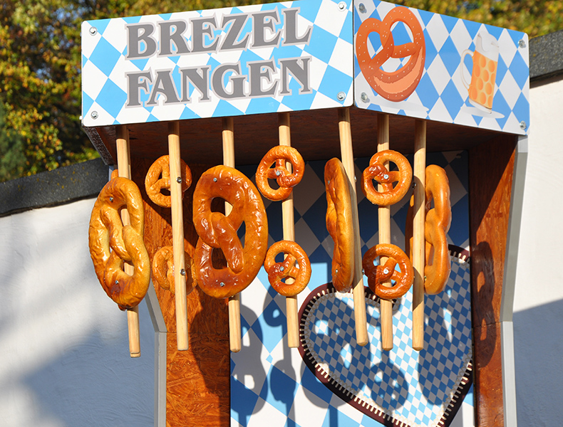 Wiesn-Spielstand „Brezel fangen“ mit Brezeln an Stäben im bayerischen Rautenmuster