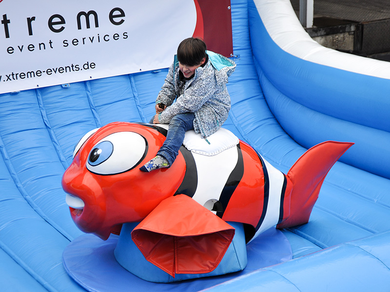Kind reitet auf einem aufblasbaren Clownfisch-Rodeo vor einem Xtreme-Banner